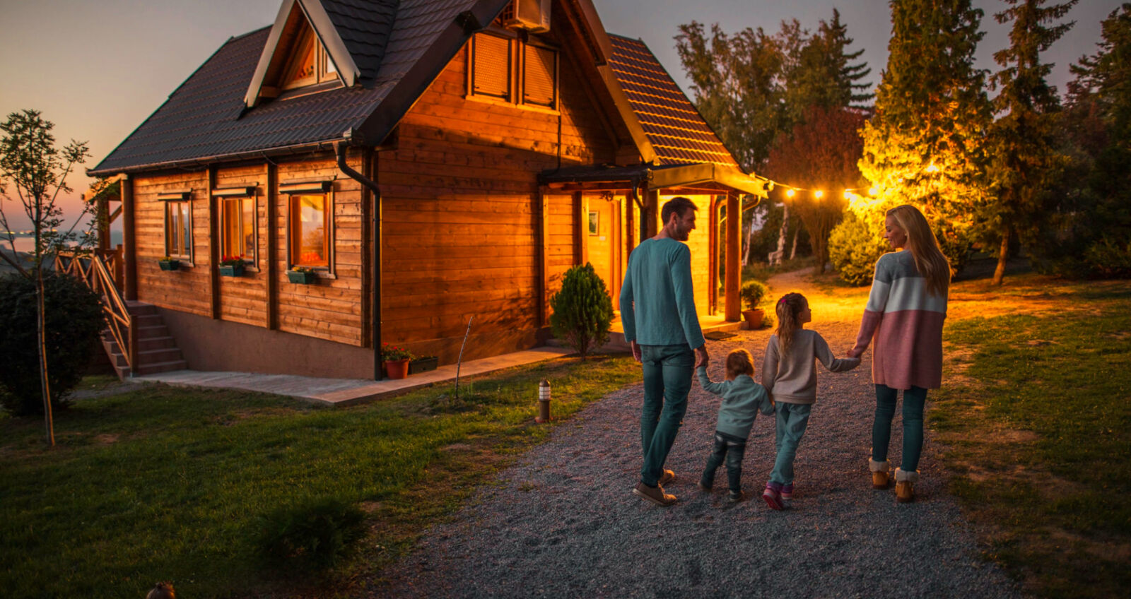 A minister's family walking hand in hand toward a warmly lit cabin at dusk